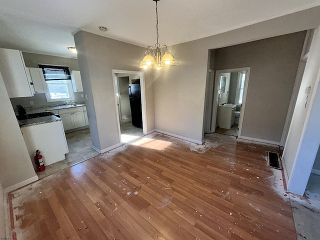 unfurnished dining area with light wood-type flooring, sink, and a chandelier