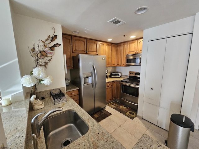 kitchen featuring light stone countertops, light tile patterned floors, stainless steel appliances, and sink