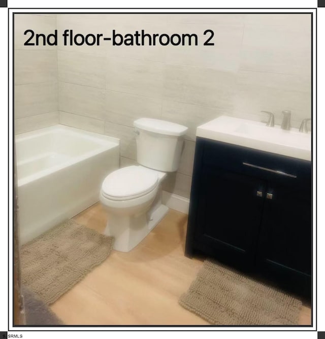 bathroom featuring tile walls, toilet, a bath, and vanity