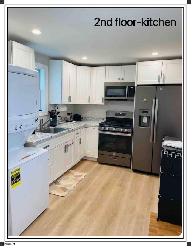 kitchen with sink, stacked washing maching and dryer, appliances with stainless steel finishes, and white cabinetry