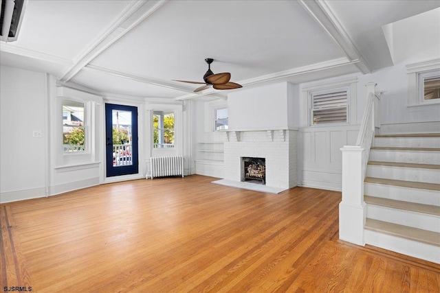 unfurnished living room featuring beam ceiling, a fireplace, light wood-style flooring, stairway, and radiator heating unit