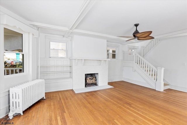 unfurnished living room with light wood finished floors, a ceiling fan, radiator heating unit, stairs, and a brick fireplace