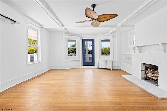 unfurnished living room featuring radiator heating unit, a wall unit AC, a fireplace, and light wood-style floors