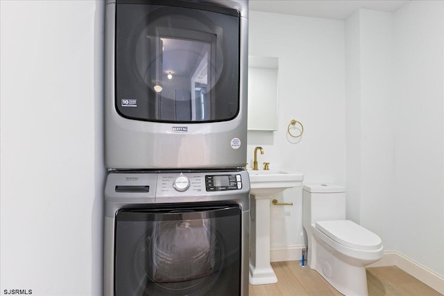 laundry area with baseboards, laundry area, a sink, and stacked washer / drying machine