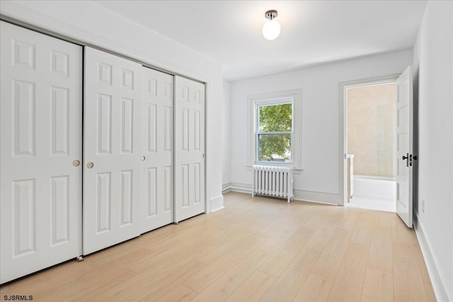 unfurnished bedroom with baseboards, a closet, light wood-type flooring, and radiator