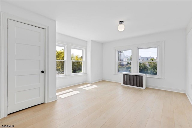 spare room with a wealth of natural light, baseboards, light wood-style flooring, and radiator heating unit