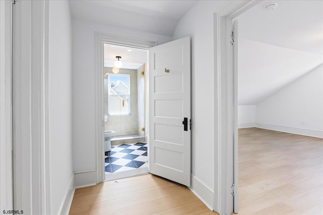 hallway featuring baseboards, vaulted ceiling, and wood finished floors