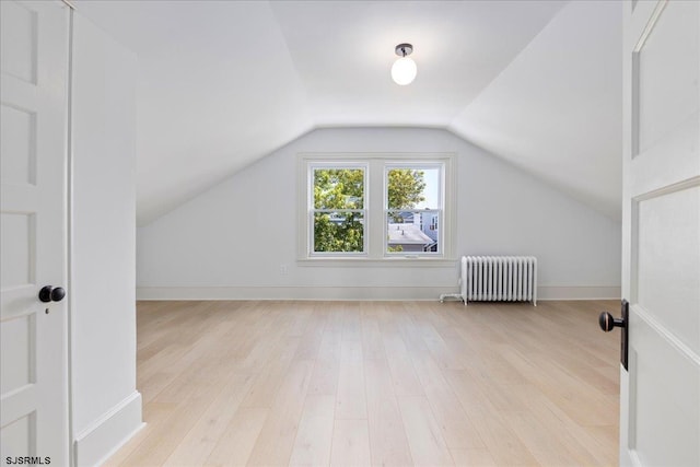 additional living space with lofted ceiling, radiator, baseboards, and light wood finished floors