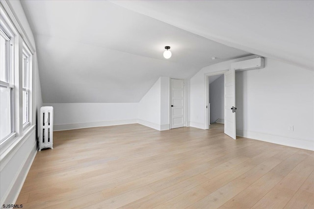 additional living space with vaulted ceiling, radiator heating unit, light wood-type flooring, and baseboards