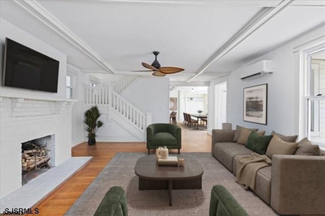 living room featuring ceiling fan, a fireplace, wood finished floors, stairs, and an AC wall unit