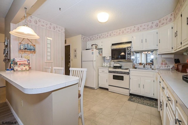 kitchen with a peninsula, white appliances, a breakfast bar, and white cabinetry