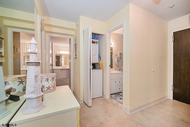 hall with a textured ceiling, stacked washer and dryer, and baseboards