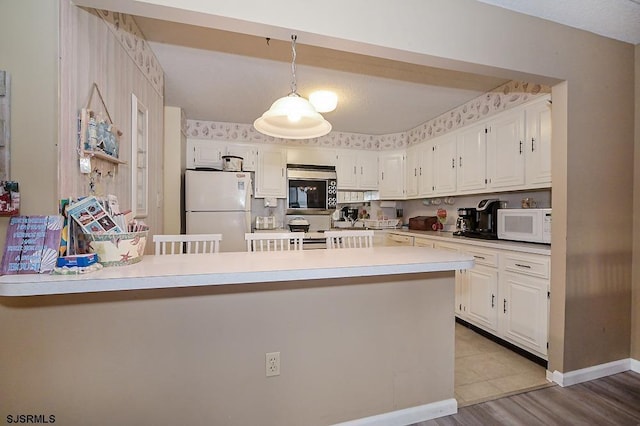 kitchen with stainless steel appliances, light countertops, white cabinetry, wood finished floors, and a peninsula