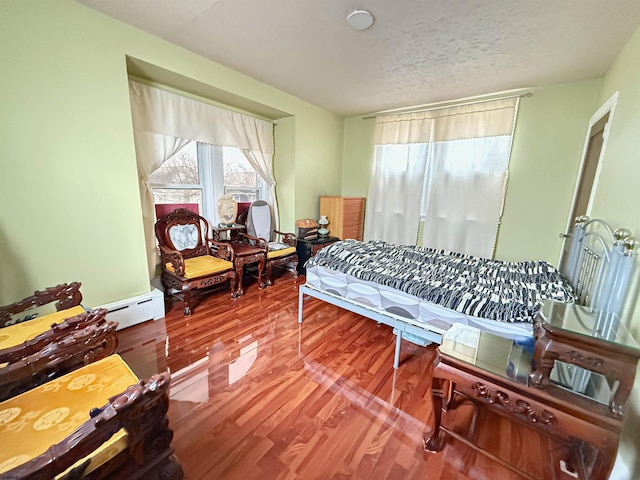 bedroom with hardwood / wood-style floors, a textured ceiling, and a baseboard heating unit