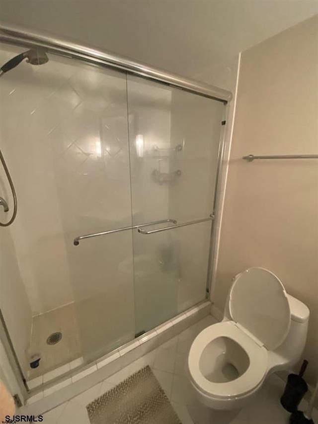 bathroom with tile patterned flooring, a shower with shower door, and toilet