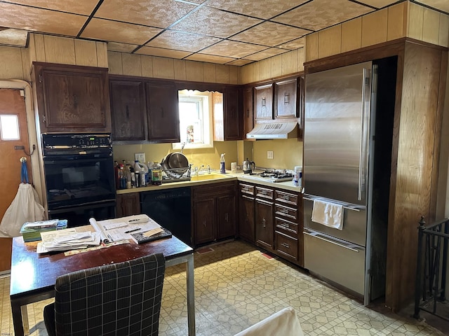 kitchen with dark brown cabinets, sink, wood walls, and black appliances