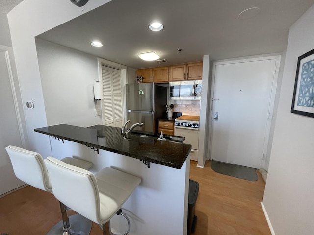 kitchen featuring backsplash, appliances with stainless steel finishes, light hardwood / wood-style floors, kitchen peninsula, and a breakfast bar area