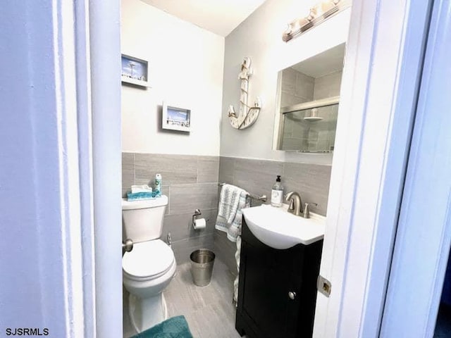 bathroom featuring hardwood / wood-style floors, vanity, toilet, tile walls, and a shower with shower door