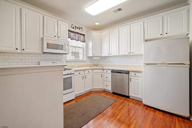 kitchen with backsplash, white appliances, sink, hardwood / wood-style flooring, and white cabinets