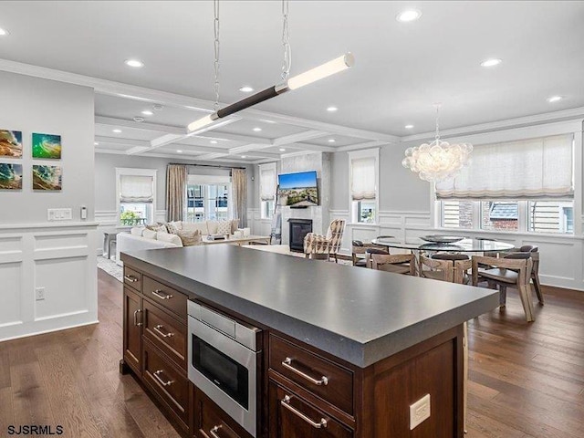 kitchen with coffered ceiling, beam ceiling, pendant lighting, a kitchen island, and stainless steel microwave