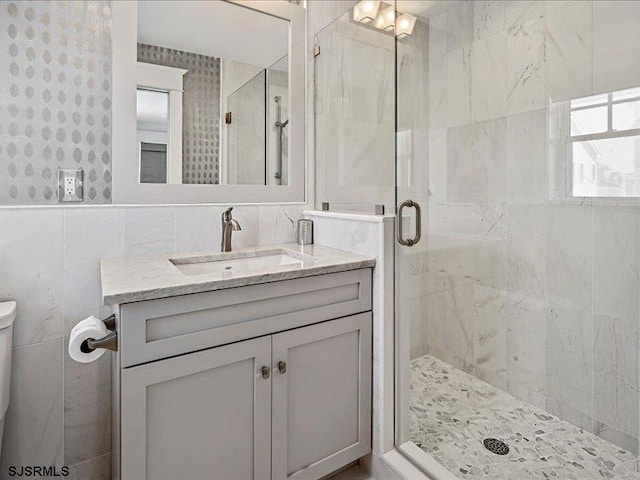 bathroom with vanity, toilet, a shower with shower door, and tile walls