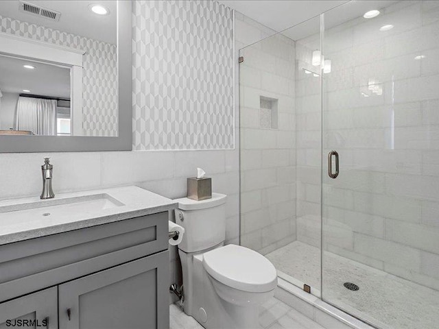 bathroom with toilet, an enclosed shower, tile walls, and vanity