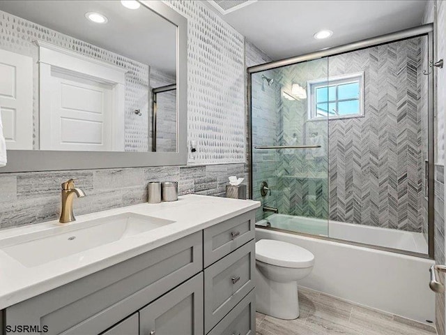 full bathroom featuring vanity, toilet, shower / bath combination with glass door, and tile walls