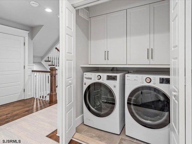 washroom featuring washing machine and dryer, light tile patterned floors, and cabinets