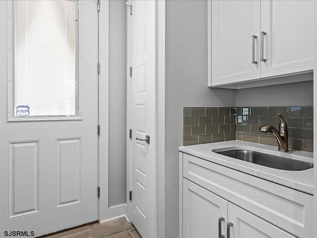 kitchen featuring sink, dark tile patterned floors, tasteful backsplash, light stone counters, and white cabinetry