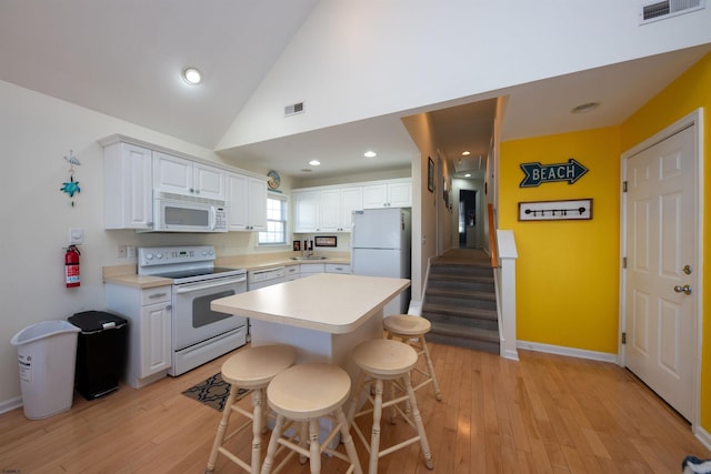 kitchen with white cabinetry, a center island, light hardwood / wood-style flooring, white appliances, and a breakfast bar area