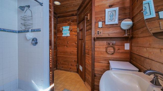 bathroom with a tile shower, sink, wooden ceiling, and wood walls