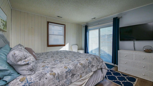 bedroom featuring access to outside, multiple windows, wooden walls, and a textured ceiling