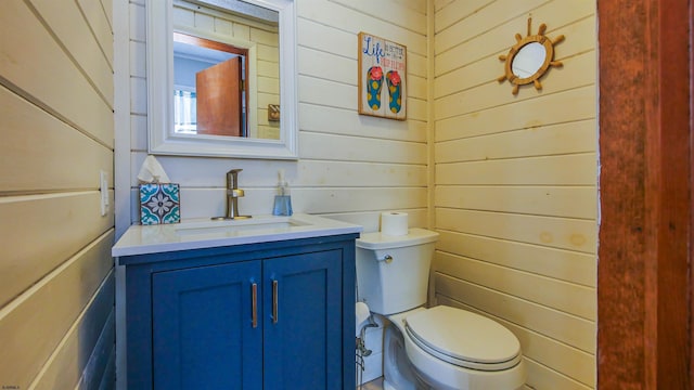 bathroom with vanity, toilet, and wooden walls