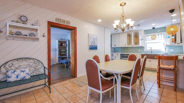 tiled dining area featuring wooden walls, sink, a textured ceiling, and a notable chandelier