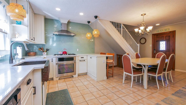 kitchen with stainless steel oven, wall chimney range hood, hanging light fixtures, and tasteful backsplash