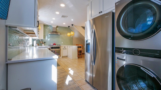 kitchen featuring appliances with stainless steel finishes, sink, pendant lighting, white cabinetry, and stacked washer / drying machine