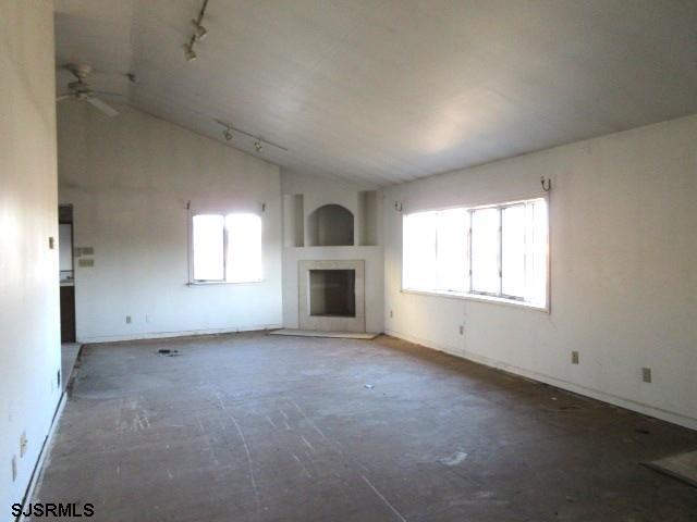 unfurnished living room featuring track lighting, ceiling fan, and vaulted ceiling