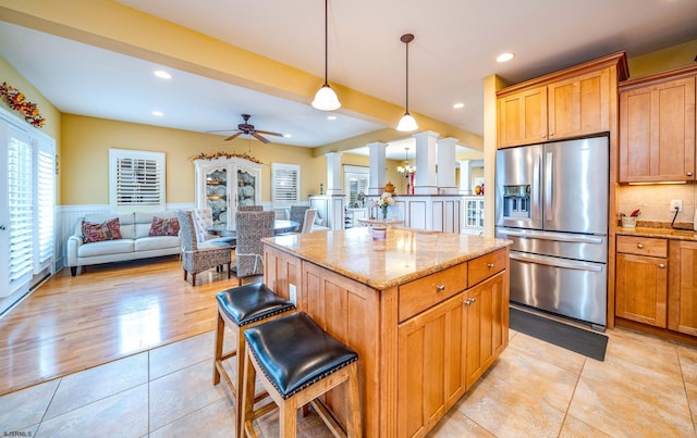 kitchen featuring pendant lighting, stainless steel fridge with ice dispenser, ornate columns, a kitchen island, and ceiling fan