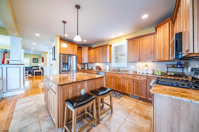 kitchen featuring a center island, light stone counters, a kitchen breakfast bar, hanging light fixtures, and appliances with stainless steel finishes