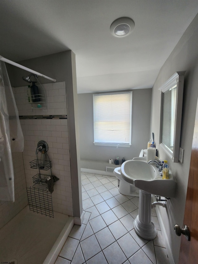 bathroom with toilet, tile patterned flooring, sink, and tiled shower