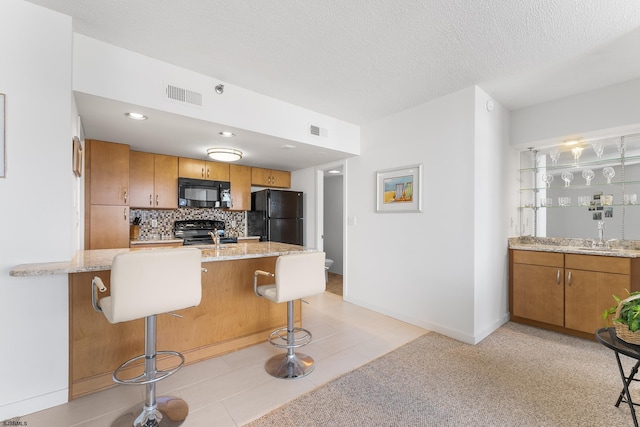 kitchen with light stone counters, a kitchen breakfast bar, light tile patterned floors, backsplash, and black appliances