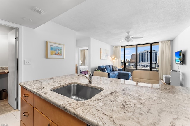 kitchen featuring sink, light tile patterned flooring, ceiling fan, a wall of windows, and light stone countertops