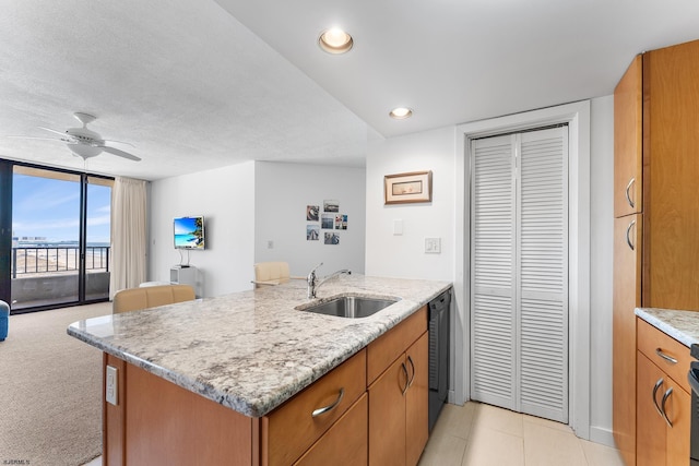 kitchen featuring sink, ceiling fan, a kitchen island with sink, and light stone counters