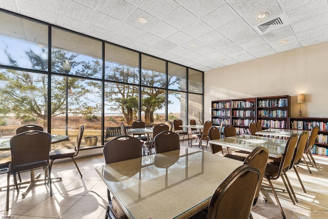 dining area with a towering ceiling, a wall of windows, a drop ceiling, and a healthy amount of sunlight