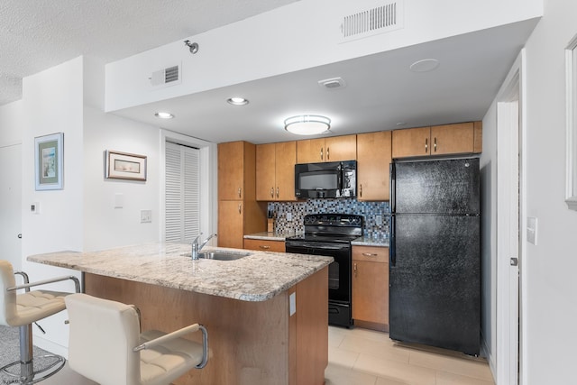 kitchen featuring a breakfast bar, black appliances, decorative backsplash, a kitchen island with sink, and sink