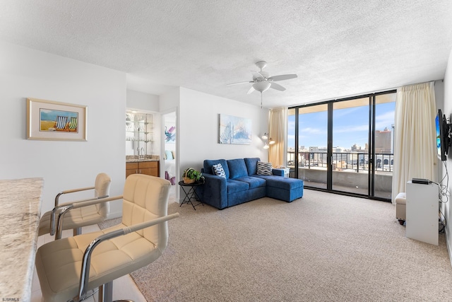 carpeted living room with a textured ceiling, ceiling fan, and a wall of windows