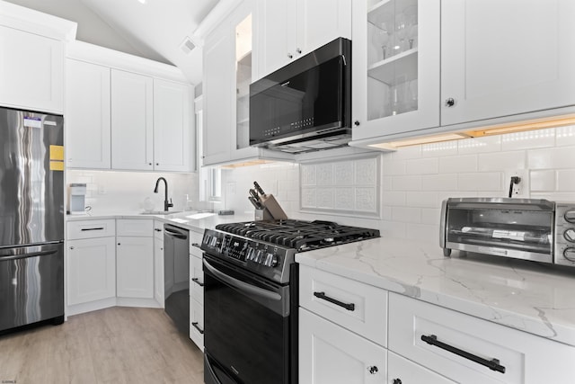 kitchen with gas stove, lofted ceiling, white cabinets, and stainless steel refrigerator