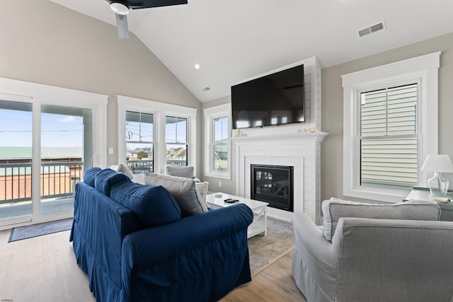 living room with ceiling fan, light hardwood / wood-style flooring, high vaulted ceiling, and a fireplace