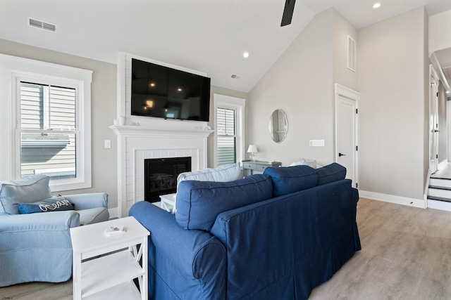 living room with a fireplace, light wood-type flooring, high vaulted ceiling, and ceiling fan