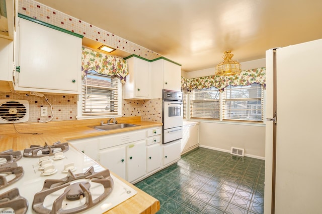 kitchen with white refrigerator, white cabinetry, sink, and a chandelier